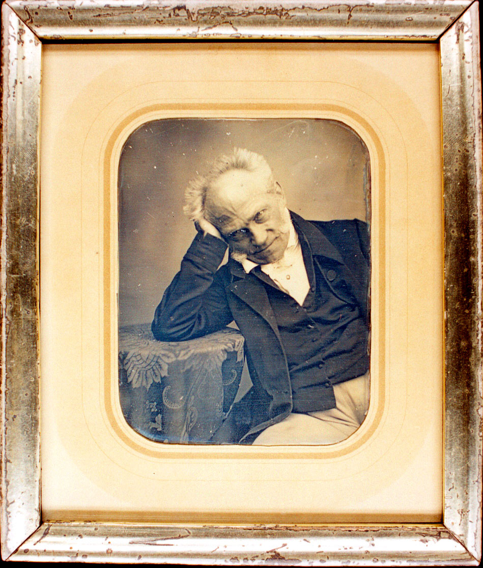 Foto-Portrait von Arthur Schopenhauer, auf dem er mit dem Ellebogen an einem Tisch lehnt, seine Hand an den Kopf fassend.